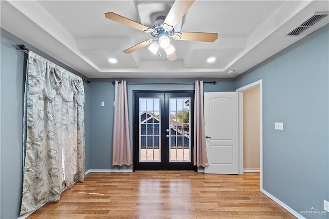 unfurnished room featuring light wood-type flooring, french doors, and a tray ceiling