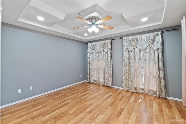 spare room with ceiling fan, light wood-type flooring, and a tray ceiling