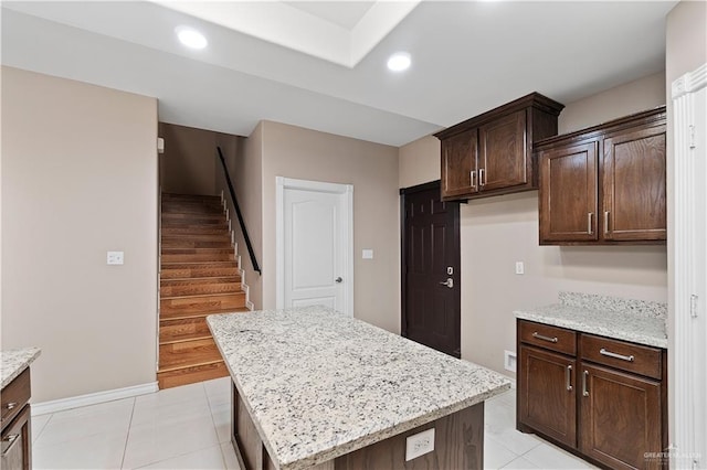 kitchen with a kitchen island, light stone counters, dark brown cabinetry, and light tile patterned floors