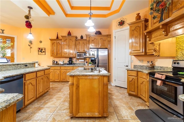 kitchen with a raised ceiling, an island with sink, hanging light fixtures, stainless steel appliances, and light stone countertops