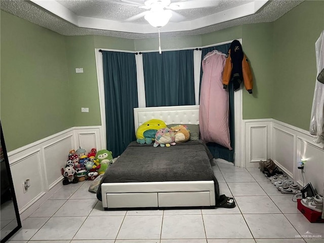 bedroom featuring a tray ceiling, a textured ceiling, a decorative wall, and light tile patterned floors