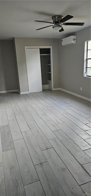 unfurnished bedroom with a wall mounted AC, light wood-type flooring, a closet, and ceiling fan