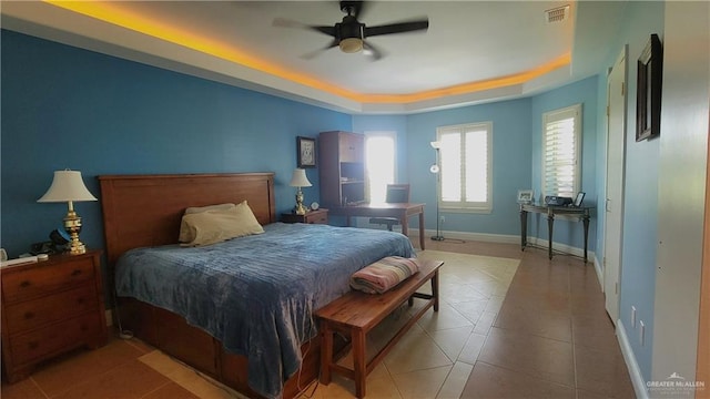 bedroom featuring ceiling fan, light tile patterned floors, and a tray ceiling