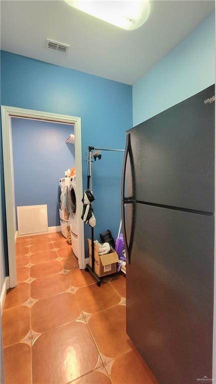 kitchen with black refrigerator, tile patterned flooring, and washing machine and clothes dryer