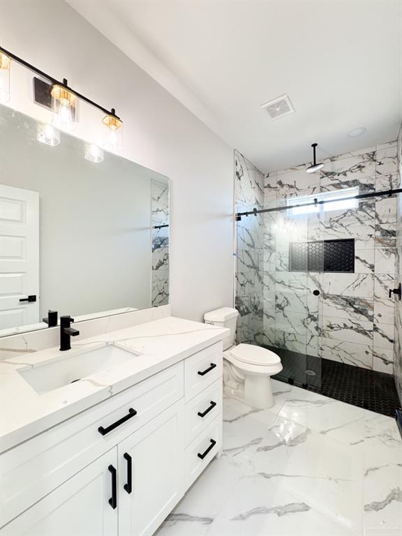 bathroom with a tile shower, vanity, and toilet