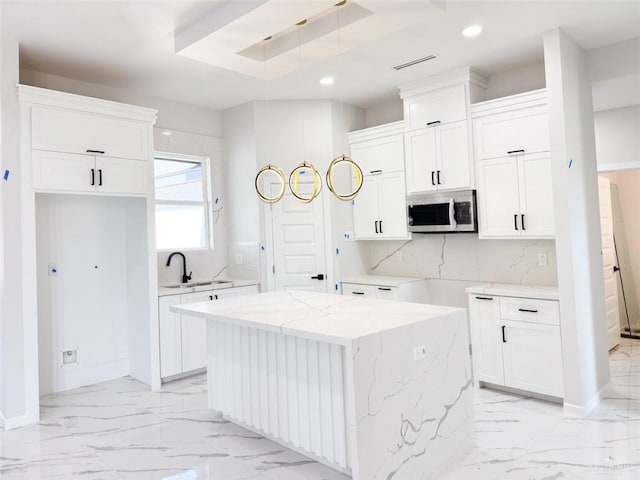 kitchen with sink, a center island, tasteful backsplash, light stone countertops, and white cabinets