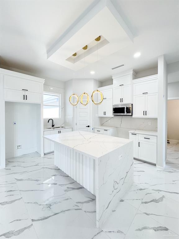 kitchen featuring white cabinetry, hanging light fixtures, light stone counters, and a center island