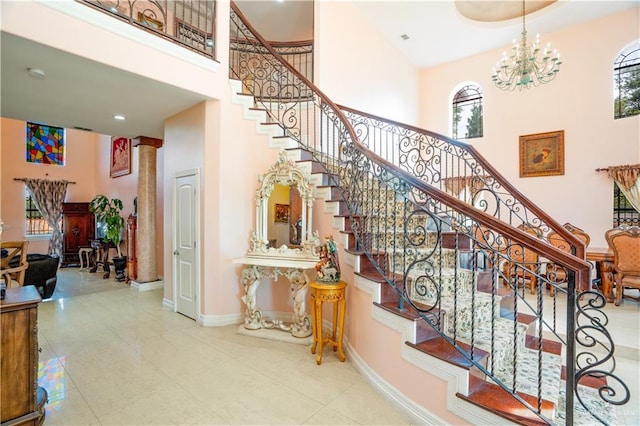 stairs with plenty of natural light, a notable chandelier, a towering ceiling, and baseboards