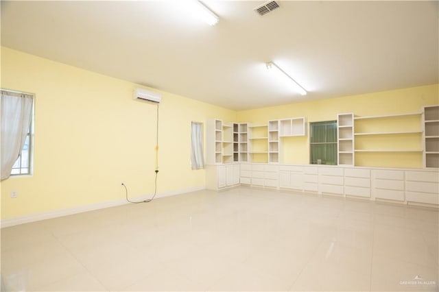 unfurnished room with an AC wall unit, baseboards, visible vents, and light tile patterned floors