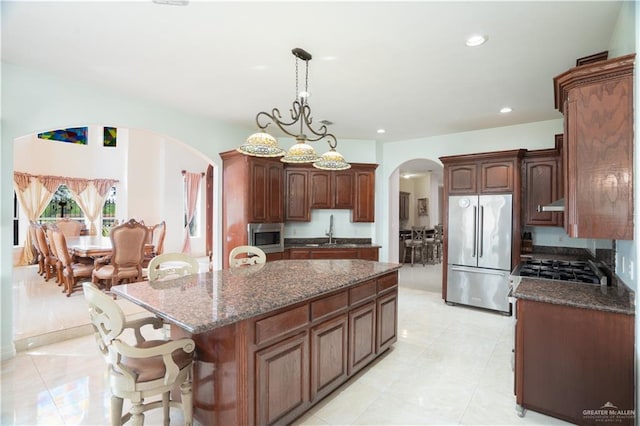 kitchen with dark stone counters, arched walkways, a center island, appliances with stainless steel finishes, and a sink