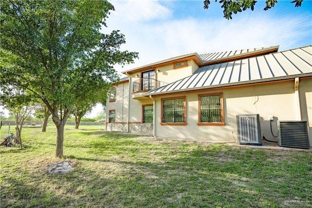 rear view of house with metal roof, a lawn, a balcony, stucco siding, and a standing seam roof