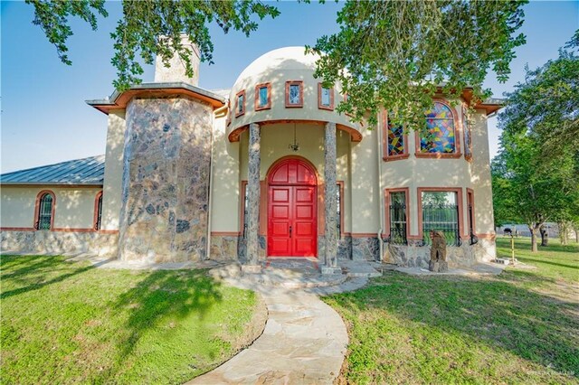 view of front of property featuring stucco siding, stone siding, a chimney, and a front lawn