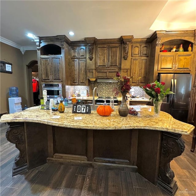 kitchen featuring dark wood-type flooring, stainless steel appliances, tasteful backsplash, light stone counters, and a large island with sink