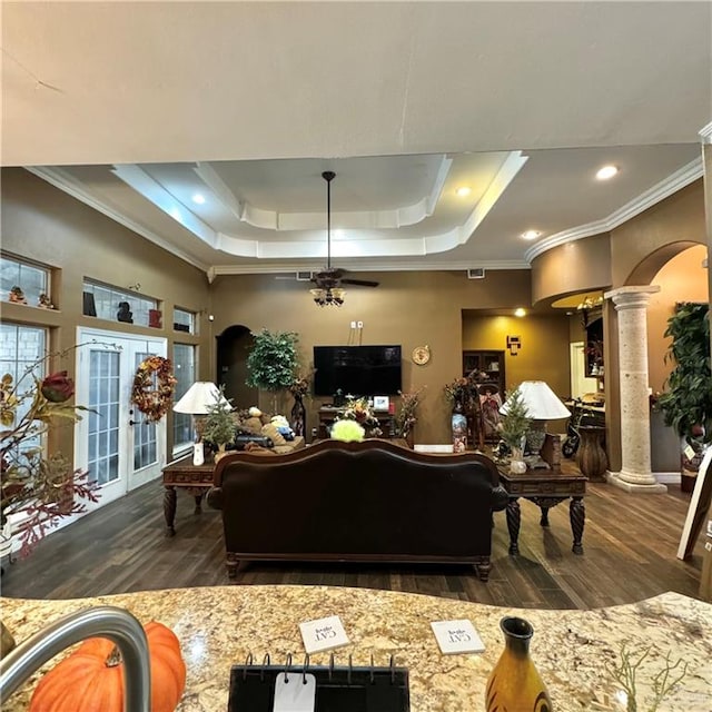 living room featuring ornamental molding, dark wood-type flooring, a tray ceiling, and decorative columns