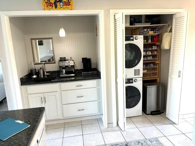 washroom featuring stacked washer and dryer, laundry area, light tile patterned floors, and a sink