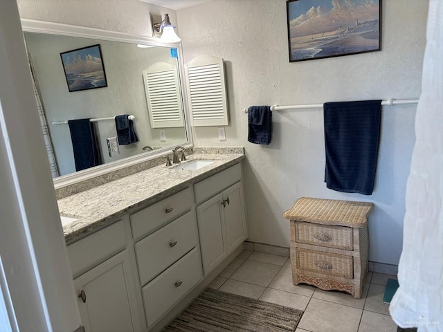 full bath featuring tile patterned flooring, baseboards, double vanity, a textured wall, and a sink