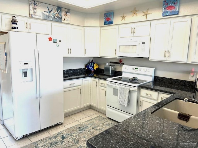 kitchen with a sink, dark stone countertops, white appliances, white cabinets, and light tile patterned floors