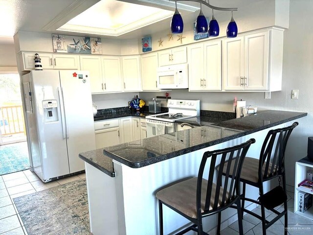 kitchen with a breakfast bar area, a peninsula, light tile patterned flooring, white appliances, and white cabinetry