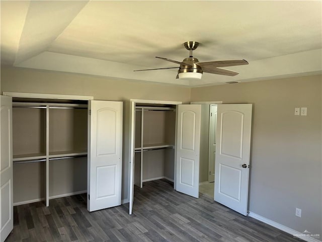 unfurnished bedroom featuring ceiling fan, dark hardwood / wood-style flooring, and two closets