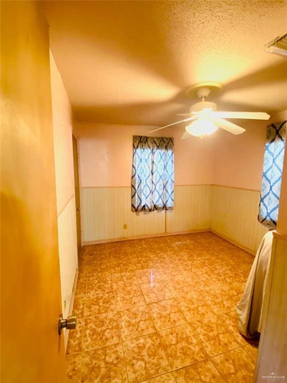 1204 E 2nd St, Weslaco, TX 78596 - tiled empty room featuring a wainscoted wall, a ceiling fan, and a textured ceiling