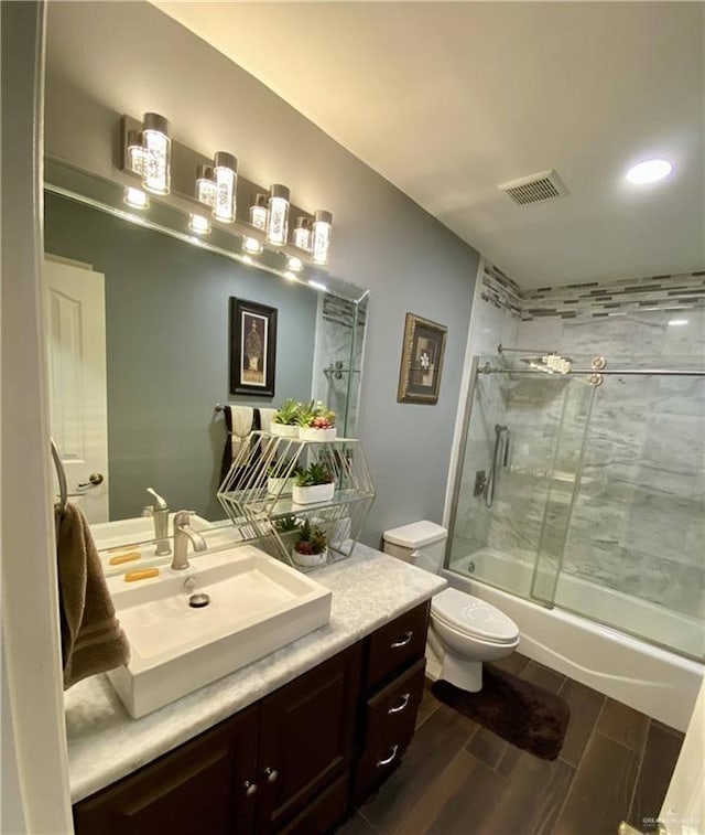 full bathroom with hardwood / wood-style flooring, toilet, vanity, and combined bath / shower with glass door