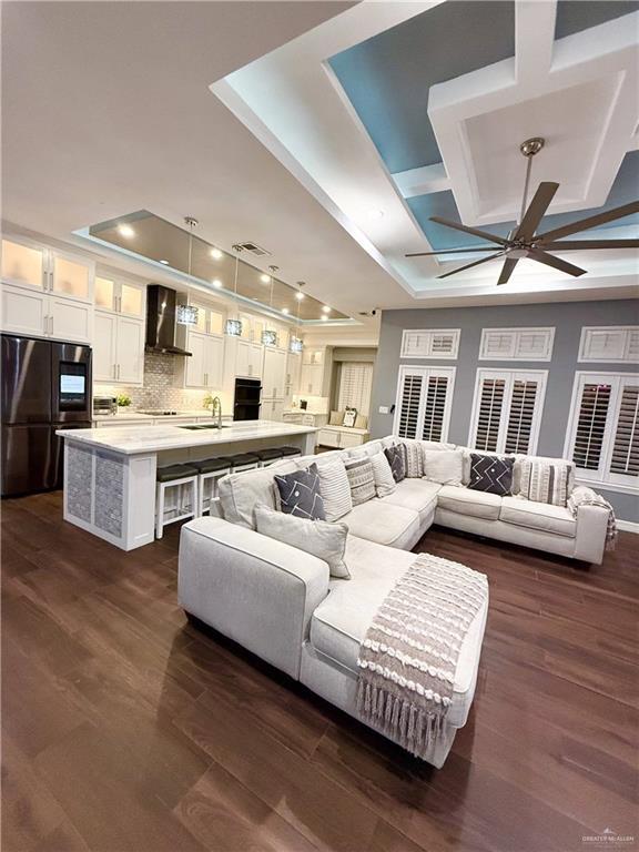 living room featuring ceiling fan, dark hardwood / wood-style flooring, sink, and a tray ceiling