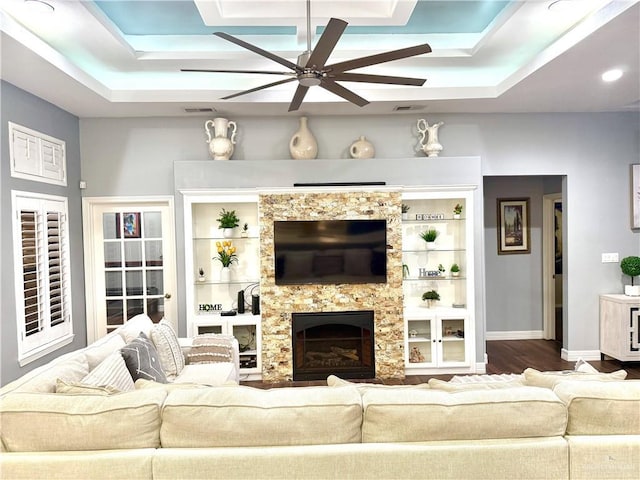 living room featuring a tray ceiling, ceiling fan, a fireplace, and wood-type flooring