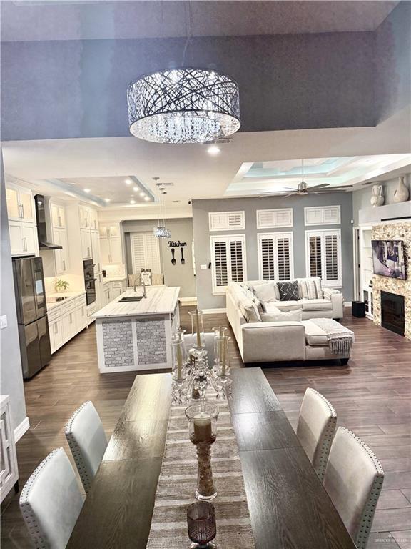 dining room featuring dark hardwood / wood-style flooring, a tray ceiling, ceiling fan, a fireplace, and a high ceiling