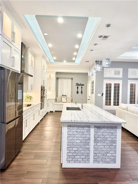 kitchen with sink, wall chimney exhaust hood, a tray ceiling, white cabinetry, and stainless steel refrigerator