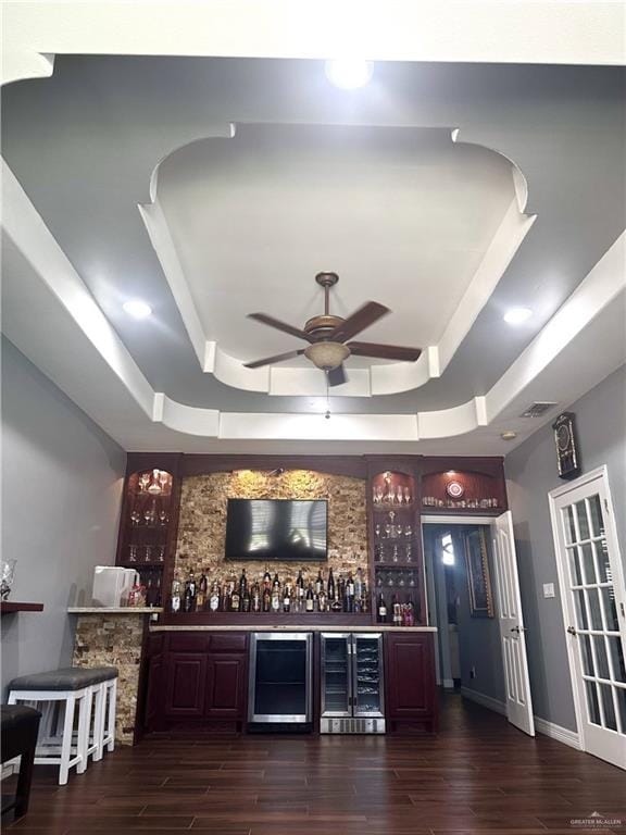 bar with dark wood-type flooring, beverage cooler, and a tray ceiling