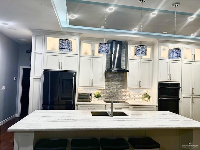 kitchen featuring a breakfast bar area, hanging light fixtures, wall chimney exhaust hood, and black appliances