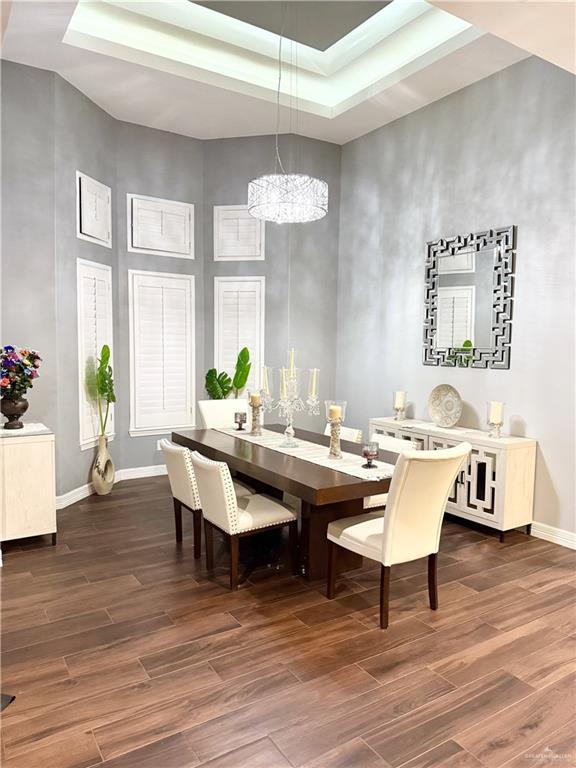 dining room featuring a notable chandelier, a towering ceiling, dark wood-type flooring, and a tray ceiling