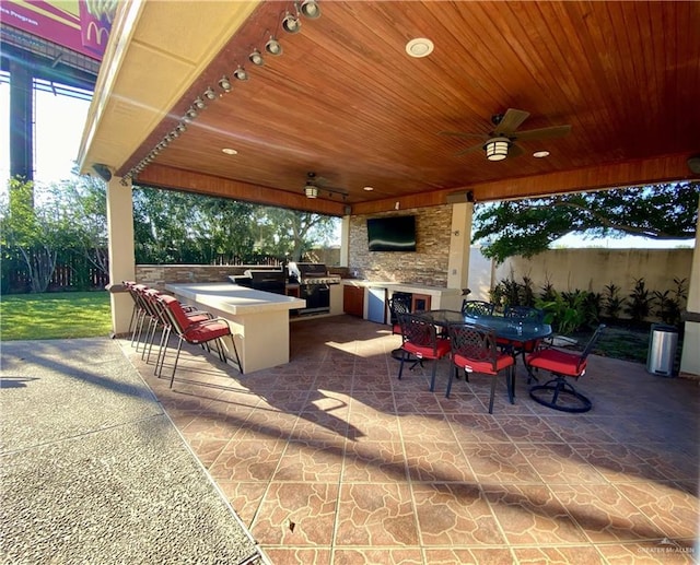 view of patio / terrace with grilling area, an outdoor stone fireplace, ceiling fan, area for grilling, and a bar