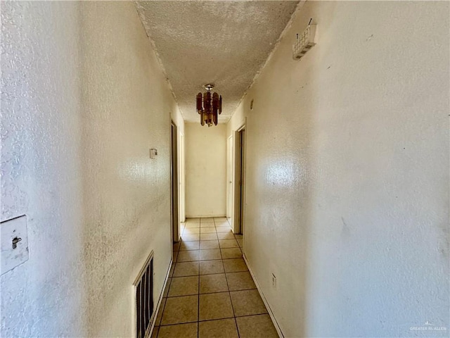 corridor featuring light tile patterned floors, visible vents, a textured ceiling, and a textured wall