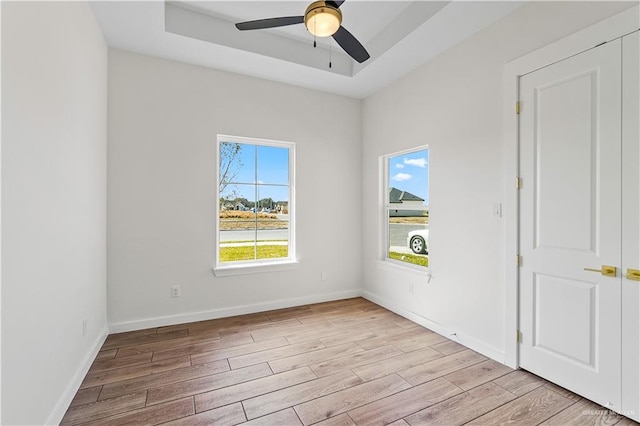 empty room with ceiling fan, light hardwood / wood-style floors, and a tray ceiling