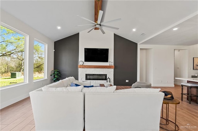 living room featuring ceiling fan, a fireplace, lofted ceiling with beams, and light wood-type flooring