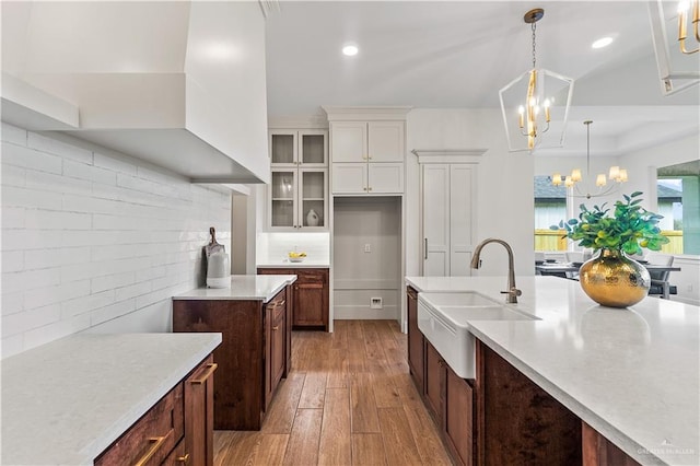 kitchen with pendant lighting, sink, a notable chandelier, light hardwood / wood-style floors, and white cabinets