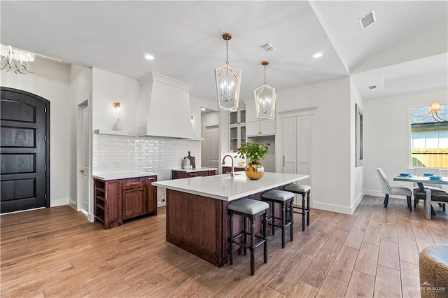 kitchen with a chandelier, a center island with sink, pendant lighting, light hardwood / wood-style floors, and white cabinets