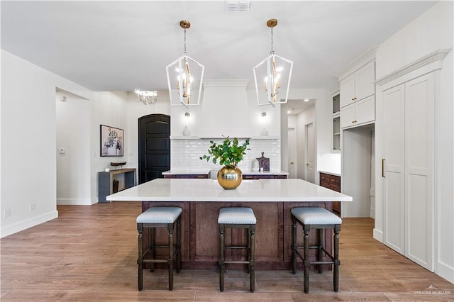 kitchen with a breakfast bar, white cabinetry, backsplash, a spacious island, and decorative light fixtures