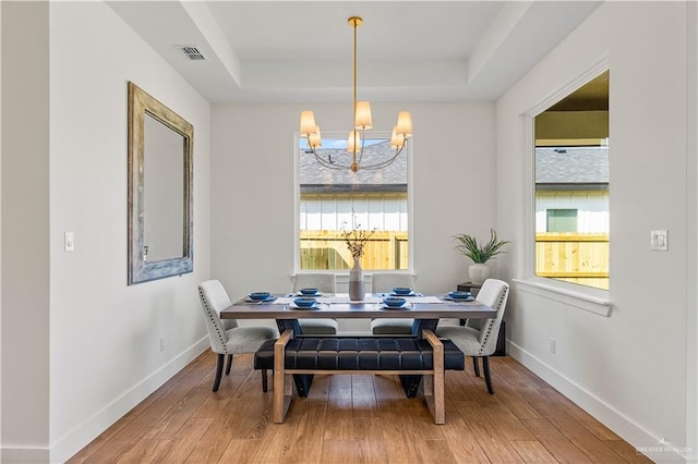 dining room featuring a raised ceiling, wood-type flooring, and an inviting chandelier