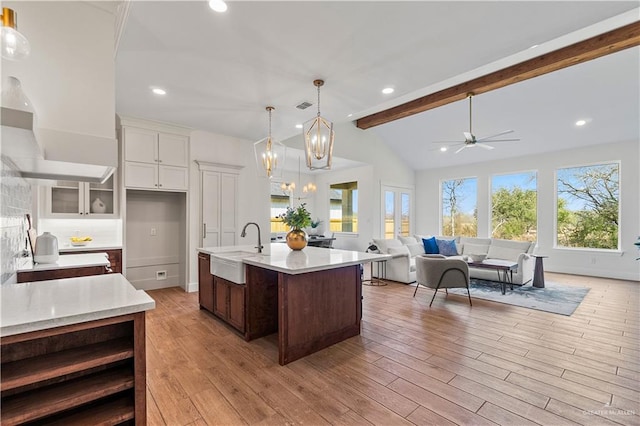 kitchen with pendant lighting, sink, a kitchen island with sink, lofted ceiling with beams, and white cabinets