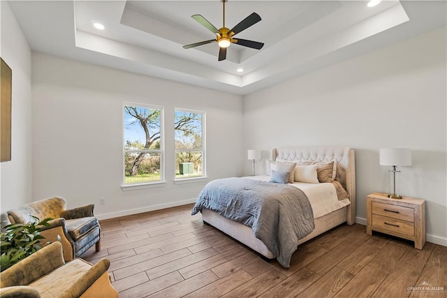 bedroom with hardwood / wood-style floors, a raised ceiling, and ceiling fan