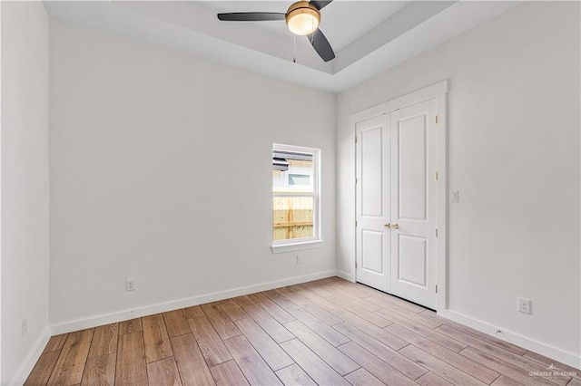 unfurnished bedroom with ceiling fan, a raised ceiling, light hardwood / wood-style floors, and a closet