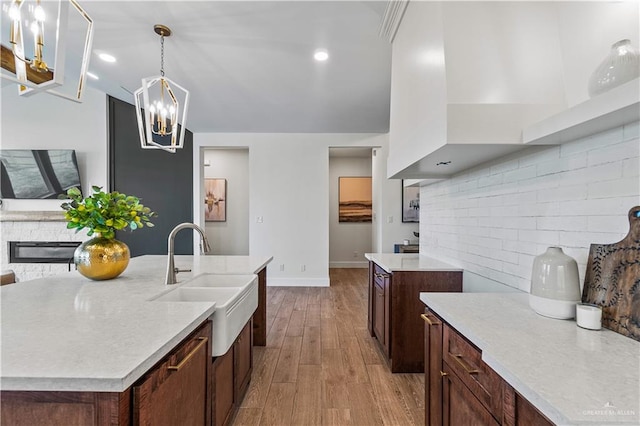 kitchen with sink, hanging light fixtures, backsplash, light hardwood / wood-style floors, and a center island with sink