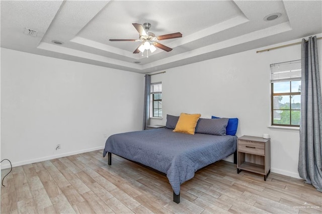 bedroom with ceiling fan, light hardwood / wood-style floors, and a tray ceiling