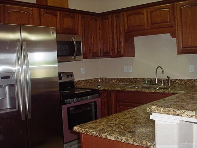 kitchen with appliances with stainless steel finishes, light stone counters, and sink