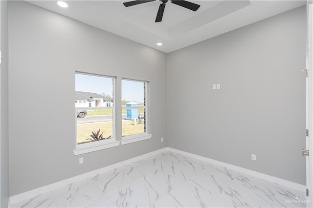 empty room with ceiling fan and a raised ceiling