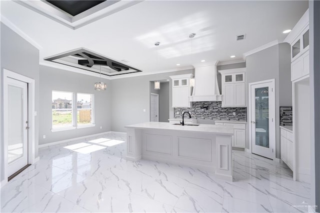 kitchen with premium range hood, pendant lighting, an island with sink, and white cabinets