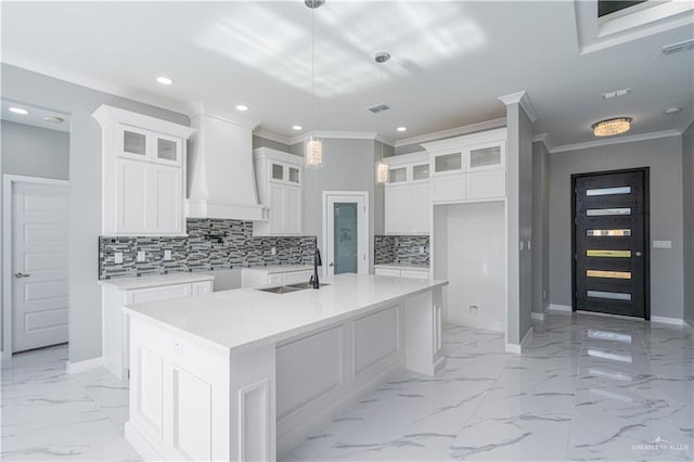 kitchen with sink, custom exhaust hood, white cabinetry, hanging light fixtures, and an island with sink