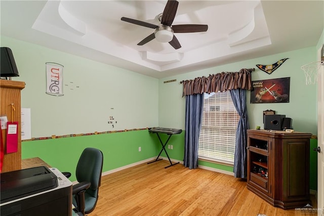 office area with a ceiling fan, baseboards, a tray ceiling, and wood finished floors